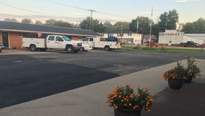 A parking lot with several white utility trucks, a building labeled "BATEMAN'S," and two potted marigold plants on the sidewalk. - Traveler's Inn Motel (Olney)