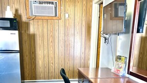 A kitchen with wooden panel walls, a refrigerator, an air conditioning unit, a wooden desk, and a chair. - Traveler's Inn Motel (Olney)