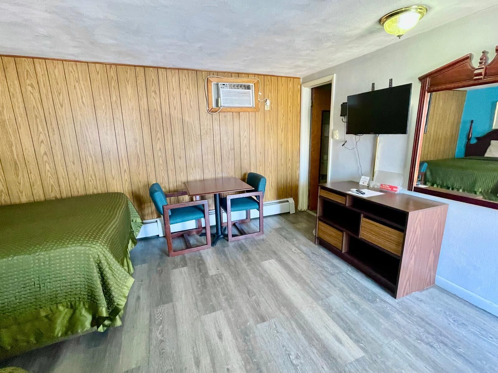 Una habitación con una cama, un escritorio con dos sillas, un televisor y un espejo.