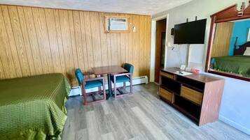 Una habitación con una cama, un escritorio con dos sillas, un televisor y un espejo.