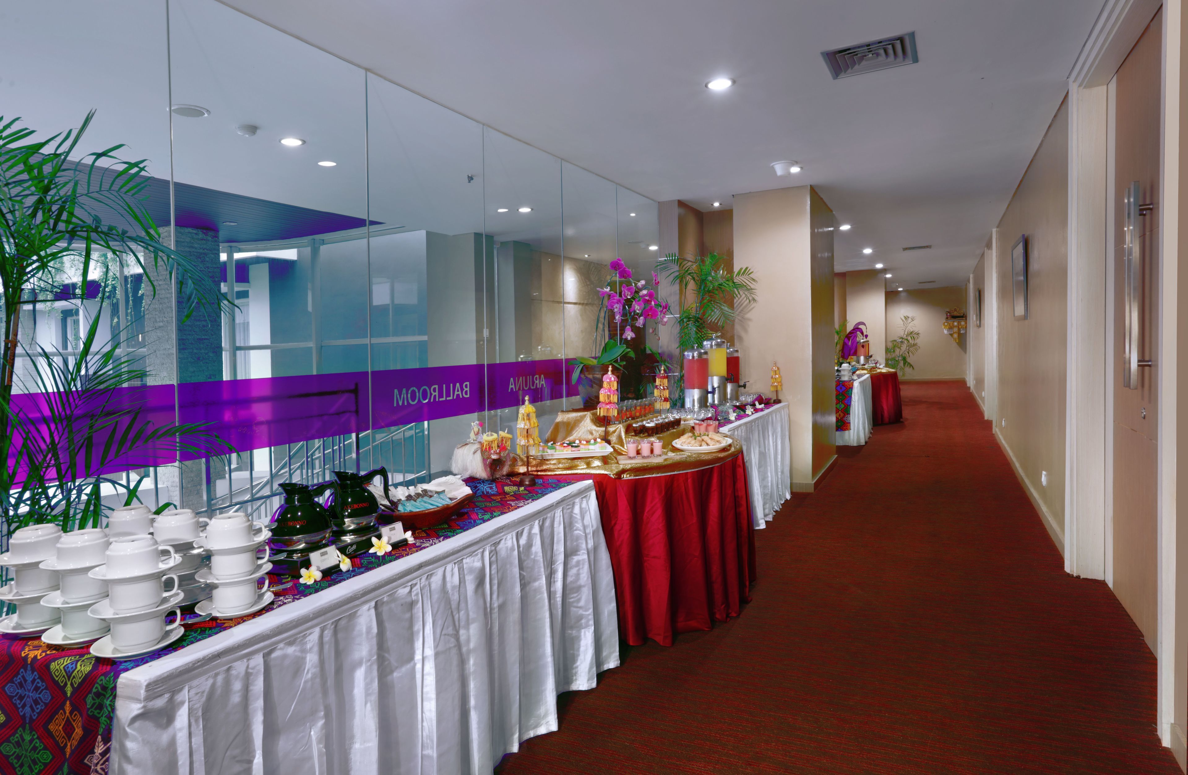 A hotel corridor with a reception area, a reception desk, and a buffet setup with various food items and dishes.