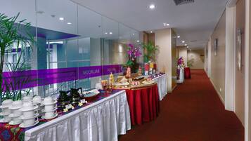 Un pasillo de hotel con zona de recepción, mostrador de recepción y un espacio para buffet con diferentes alimentos y platos.
