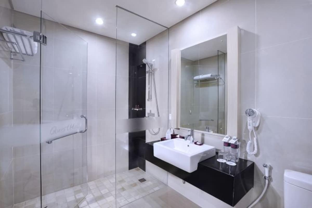 A modern bathroom with a glass shower enclosure, a white sink with a black countertop, and a large mirror above the sink.