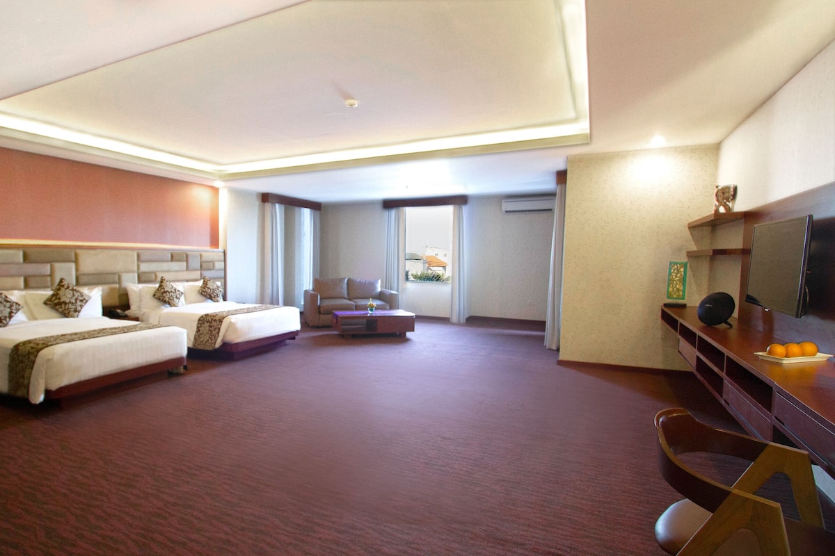 Ett hotellrum med två sängar, en soffa, ett soffbord, en tv och ett skrivbord med en dator.