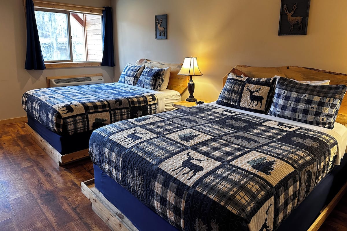 A bedroom with two beds, a window with curtains, a lamp, and wall decorations.