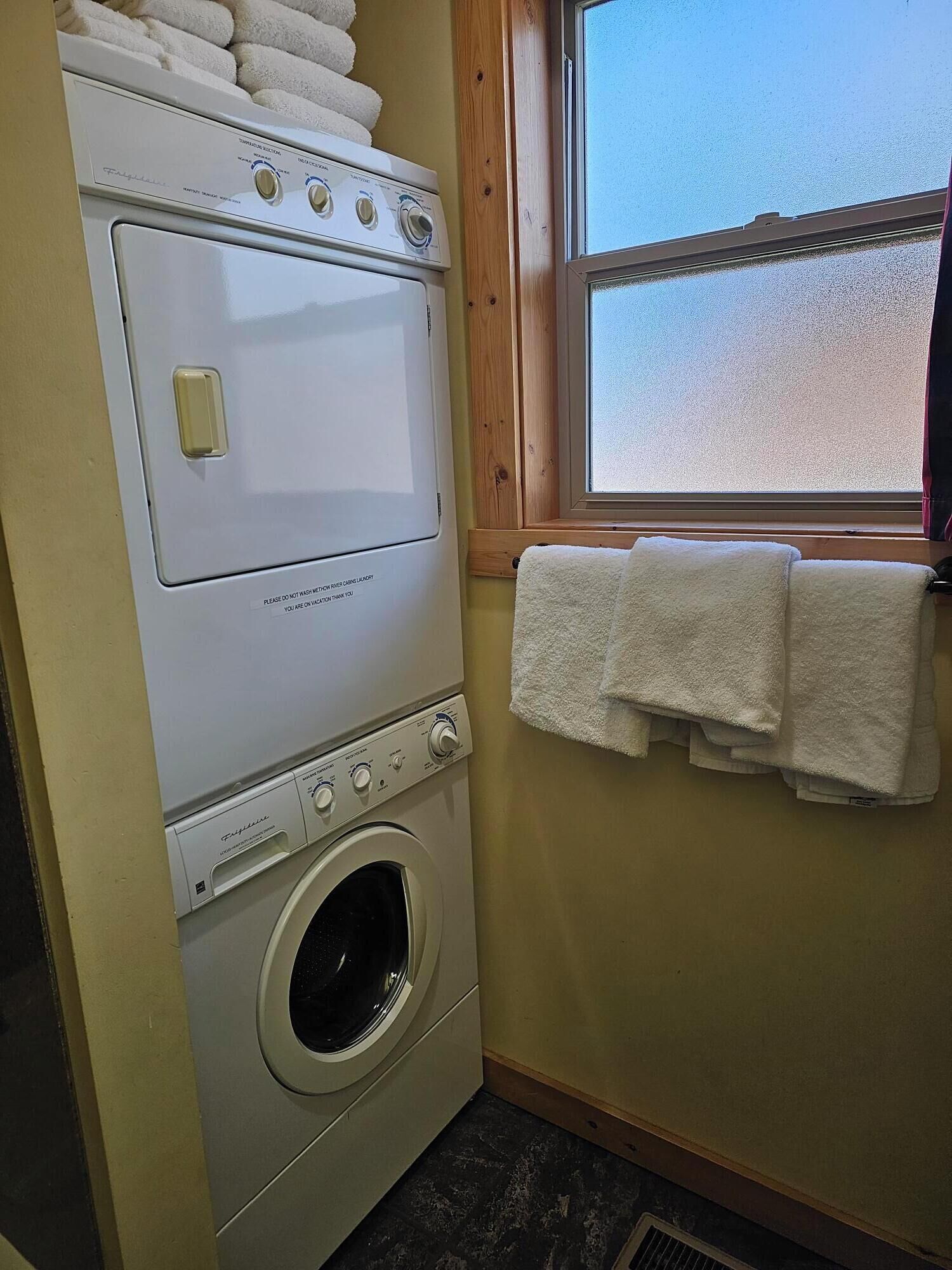 A laundry room with a front-loading washer and dryer, a window with a view, and a towel rack with folded towels.