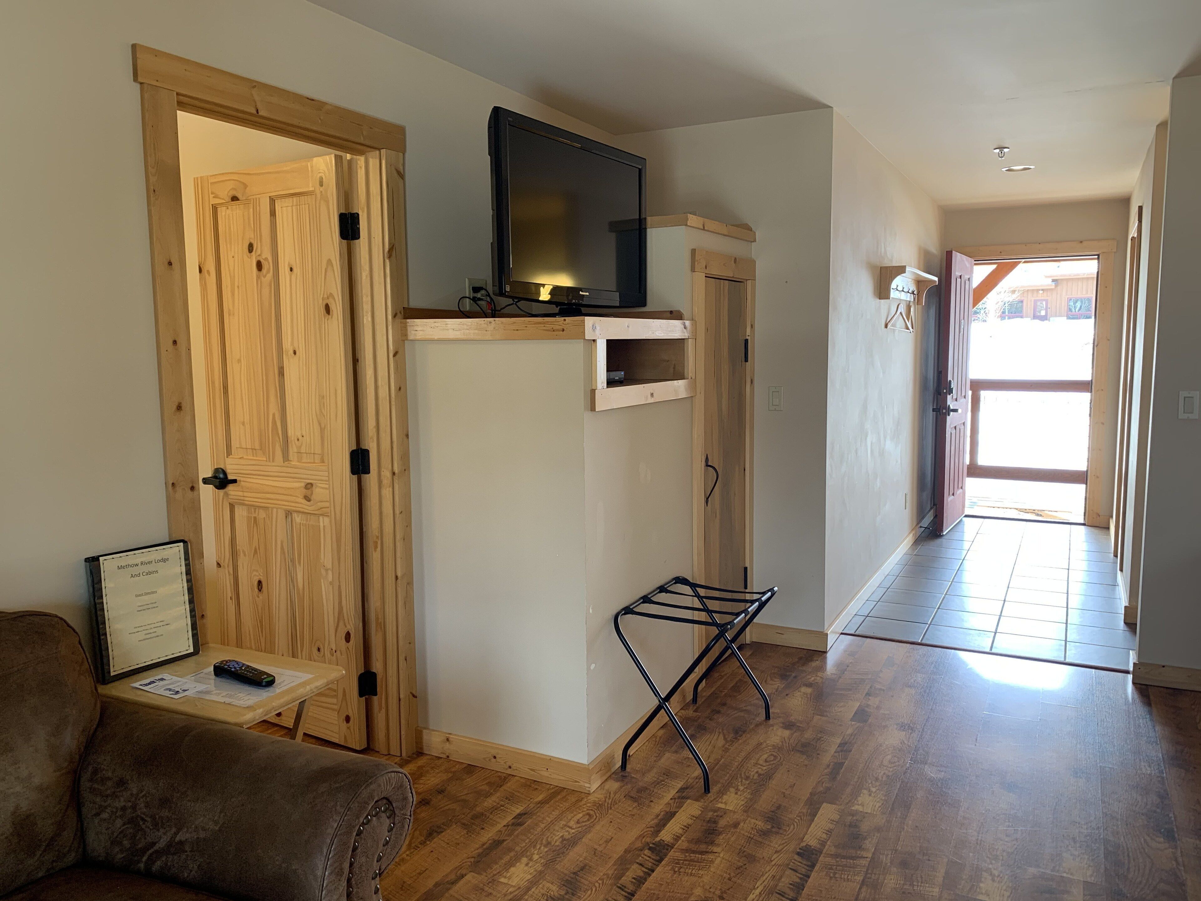 Una habitación con puertas de madera, un televisor sobre una estantería de madera, una mesita con un control remoto y un perchero metálico negro.