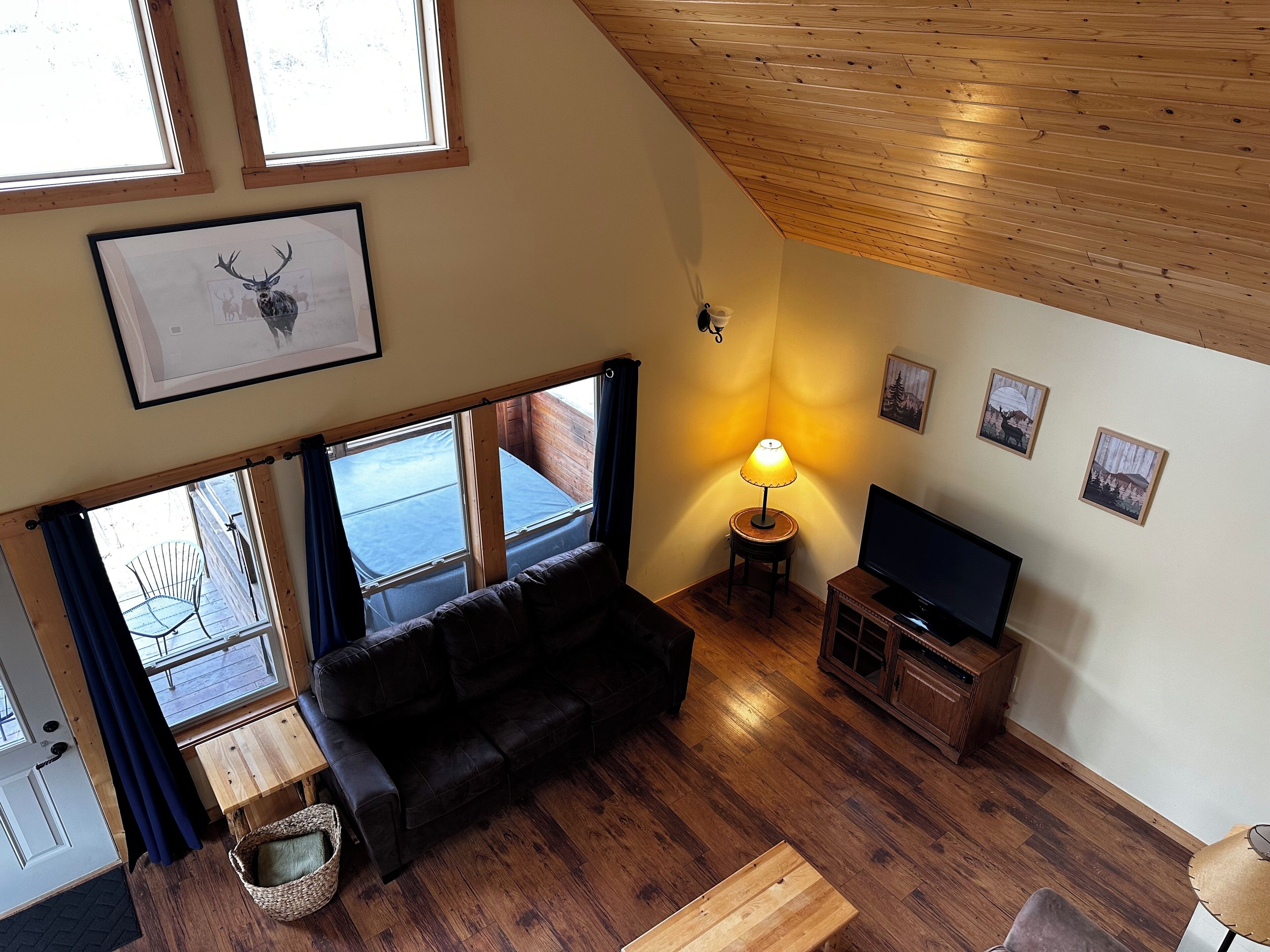 A cozy living room with a wooden ceiling, a sofa, a TV stand, and a lamp.