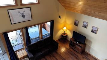 A cozy living room with a wooden ceiling, a sofa, a TV stand, and a lamp.