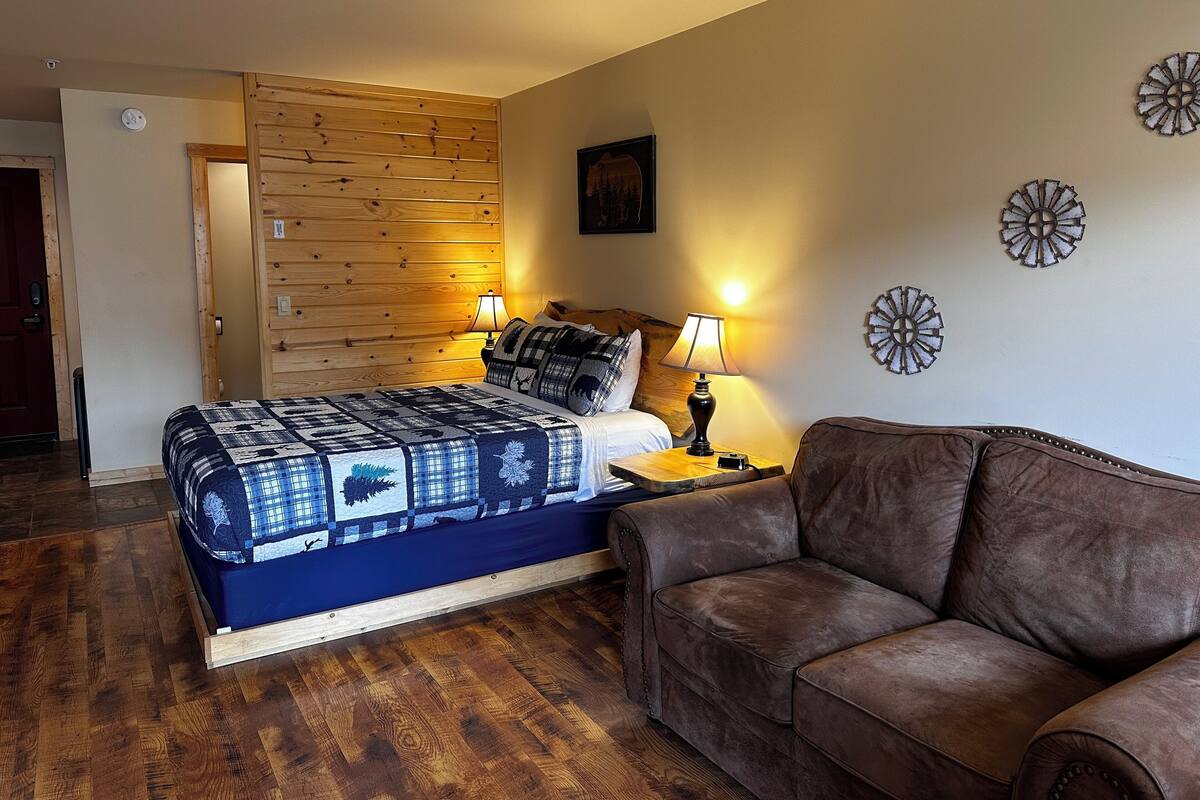 A bedroom with a wooden headboard, a bed with a blue and white quilt, a brown leather sofa, and decorative wall art.