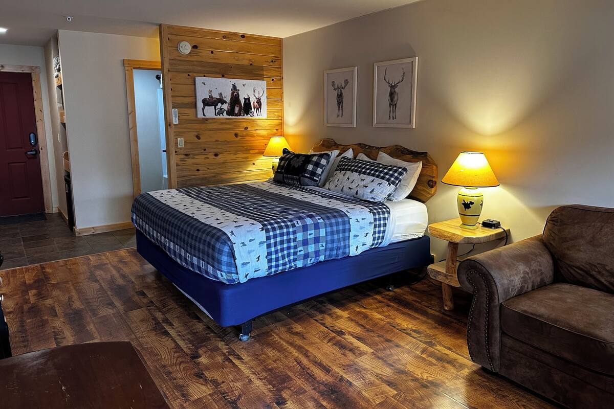 A bedroom with a wooden headboard, a bed with checkered bedding, two wall-mounted lamps, and framed deer pictures.