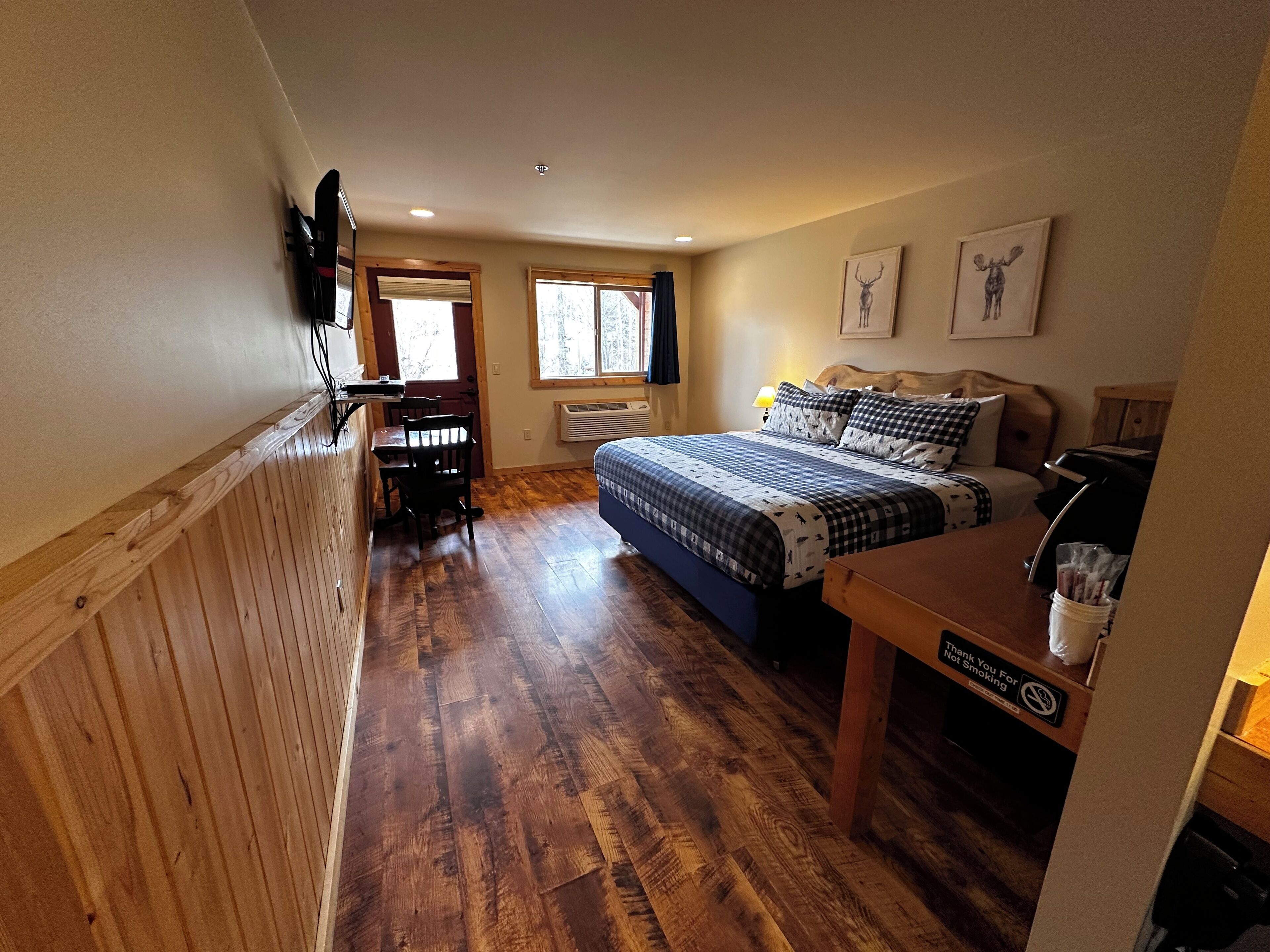 A bedroom with a bed, a desk, a chair, a window, and a wall-mounted TV.