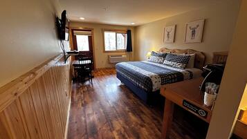 A bedroom with a bed, a desk, a chair, a window, and a wall-mounted TV.