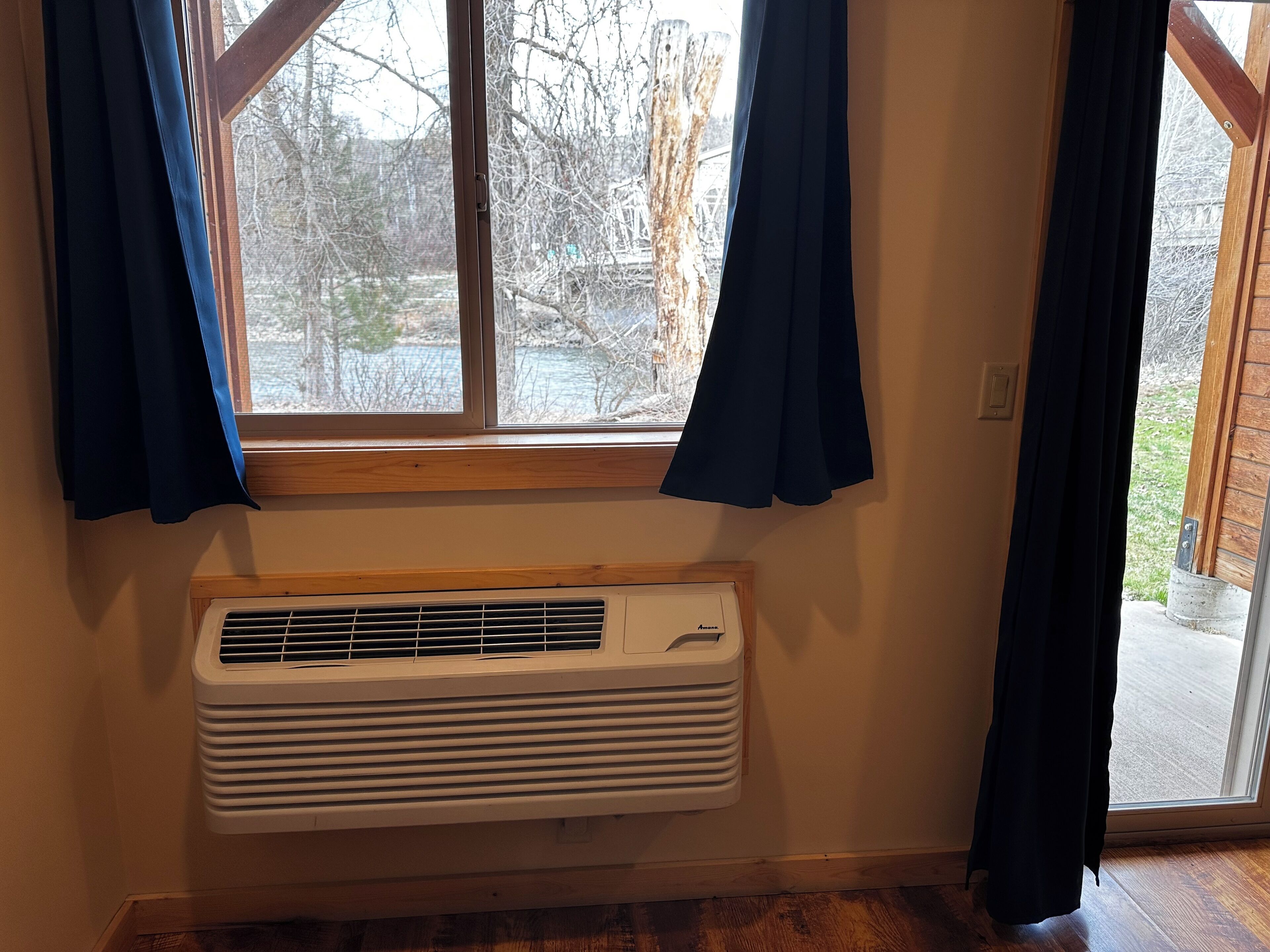 A room with a window, a wall-mounted air conditioner, and a door leading outside.