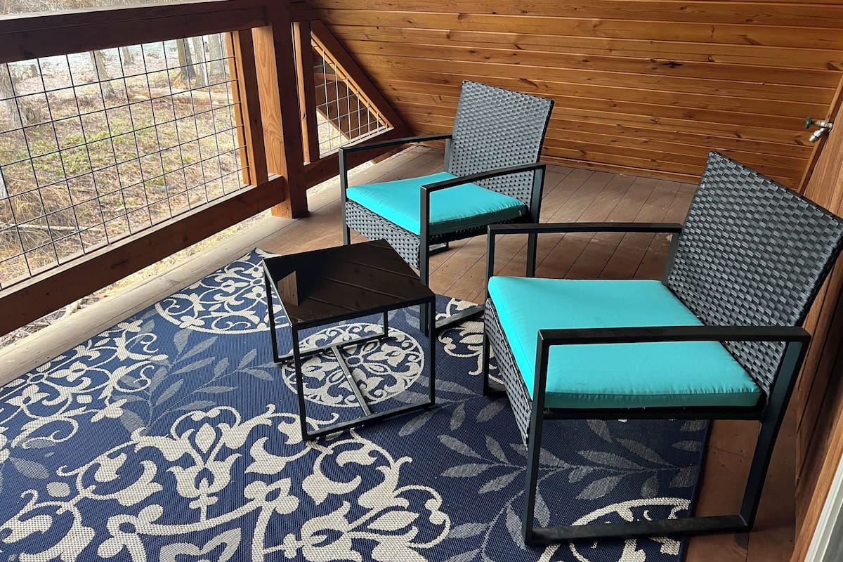 A covered outdoor seating area with a patterned floor, wooden walls, and a view through a wire mesh.