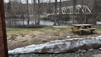 Uitzicht op een picknicktafel en een met sneeuw bedekte grond, met een rivier en bomen op de achtergrond.