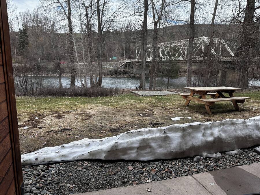 Uitzicht op een picknicktafel en een met sneeuw bedekte grond, met een rivier en bomen op de achtergrond.