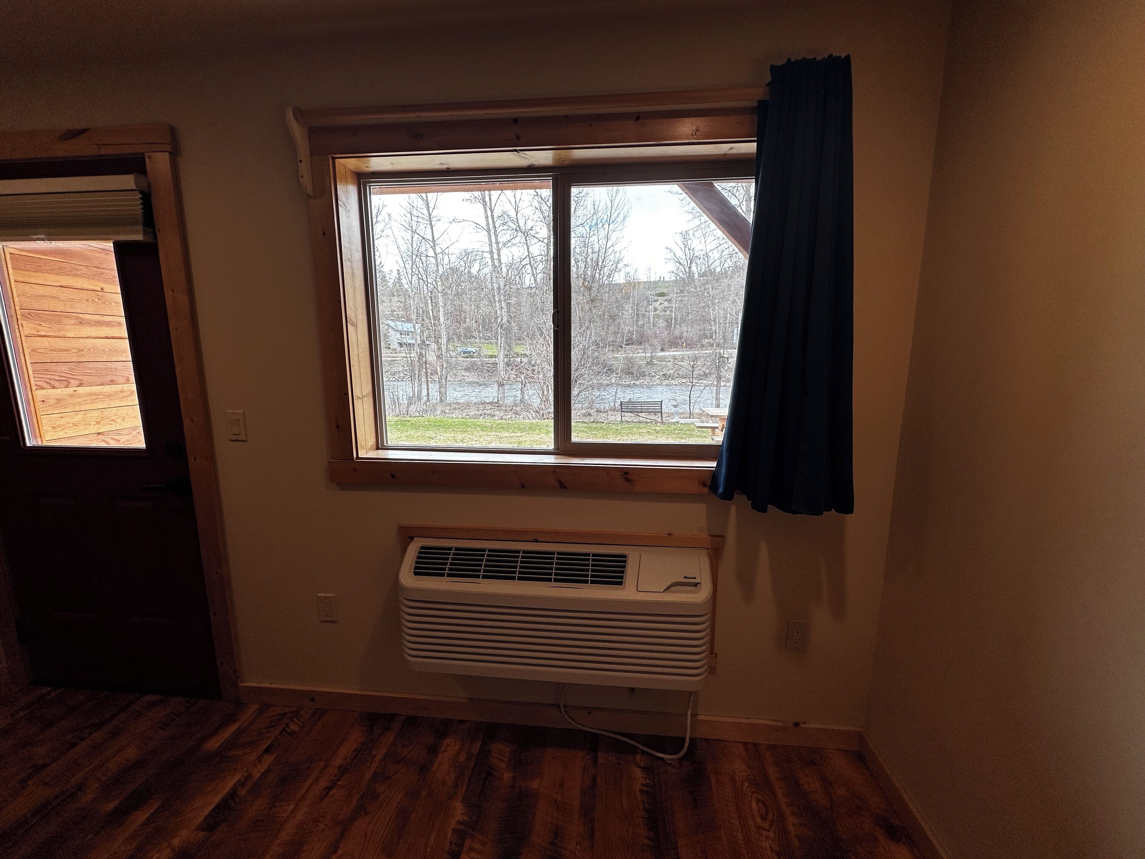 Una habitación con ventana, aire acondicionado y suelo de madera.