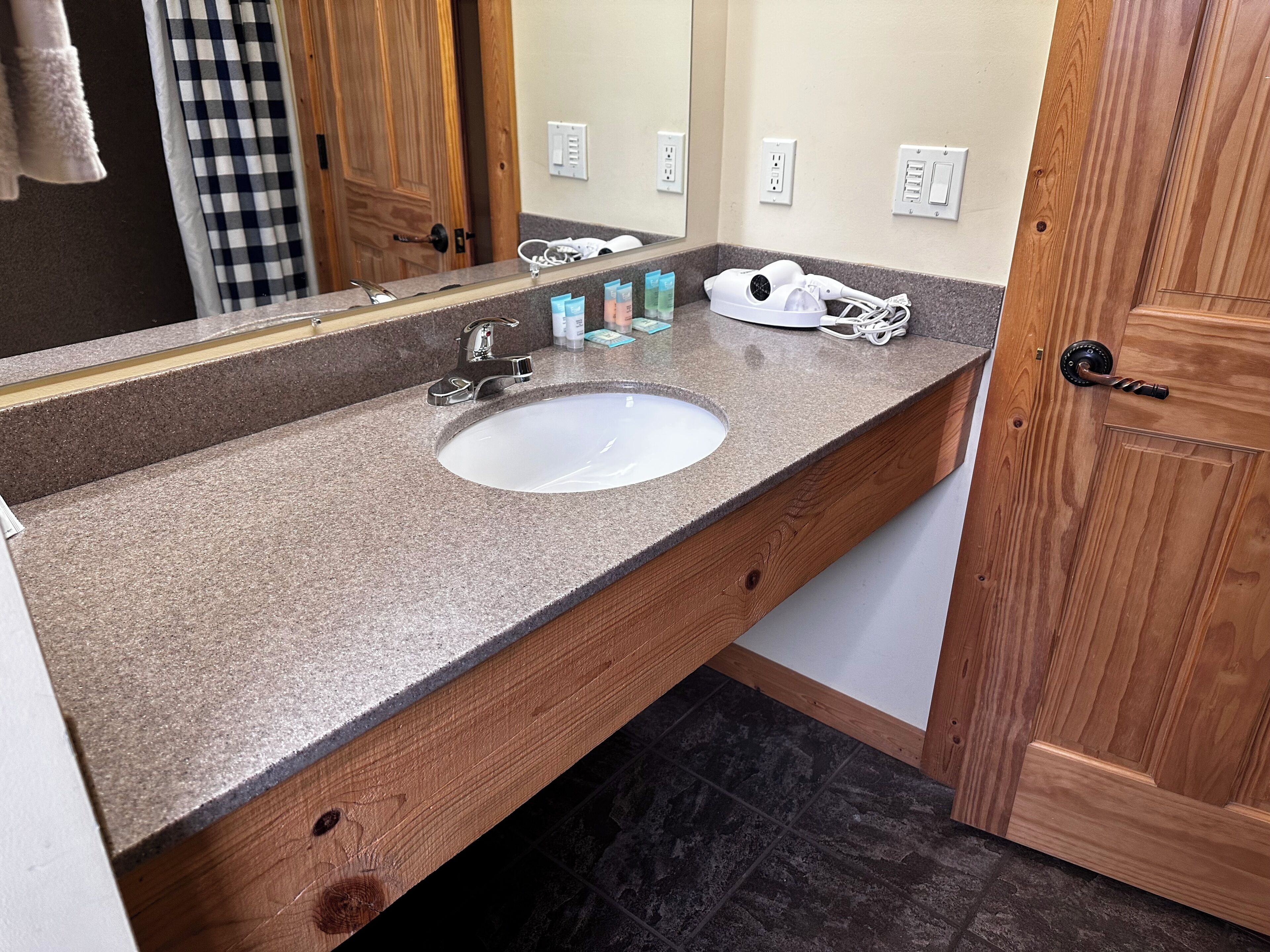 A bathroom with a granite countertop, a white sink, a mirror, and a wooden door.