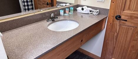 A bathroom with a granite countertop, a white sink, a mirror, and a wooden door.