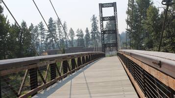 A wooden pedestrian bridge with metal railings, surrounded by trees.