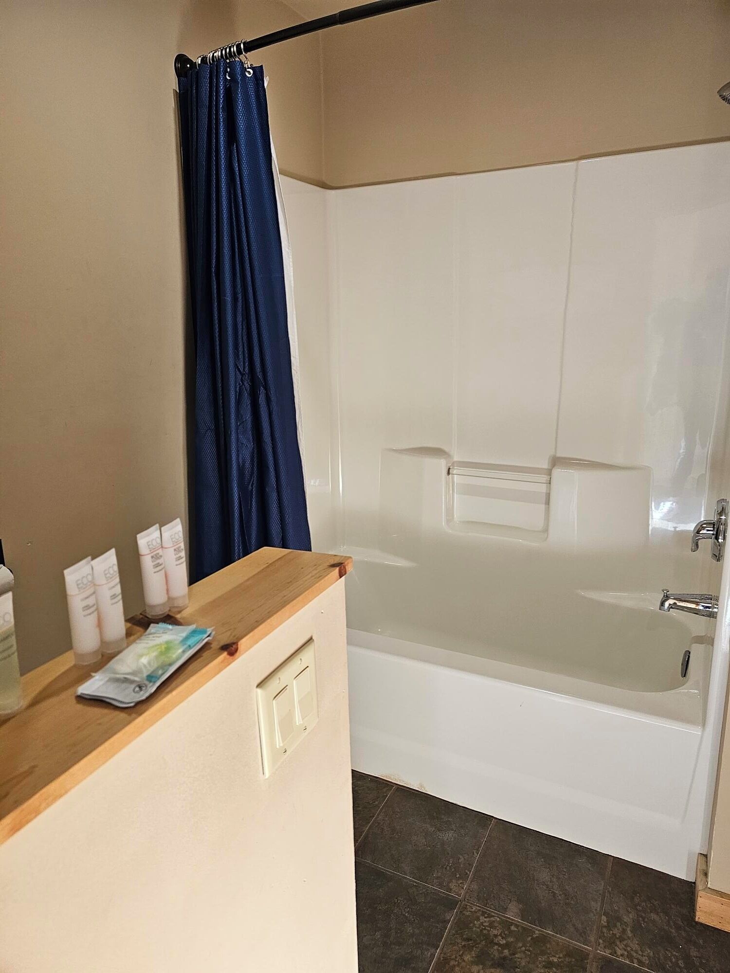 A bathroom with a bathtub, a wooden counter with toiletries, and a blue shower curtain.