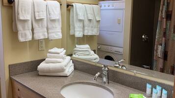 A bathroom with a sink, mirror, towels, and toiletries.