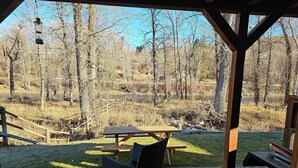 A wooden deck with a picnic table and chairs, overlooking a natural landscape with trees and a body of water.