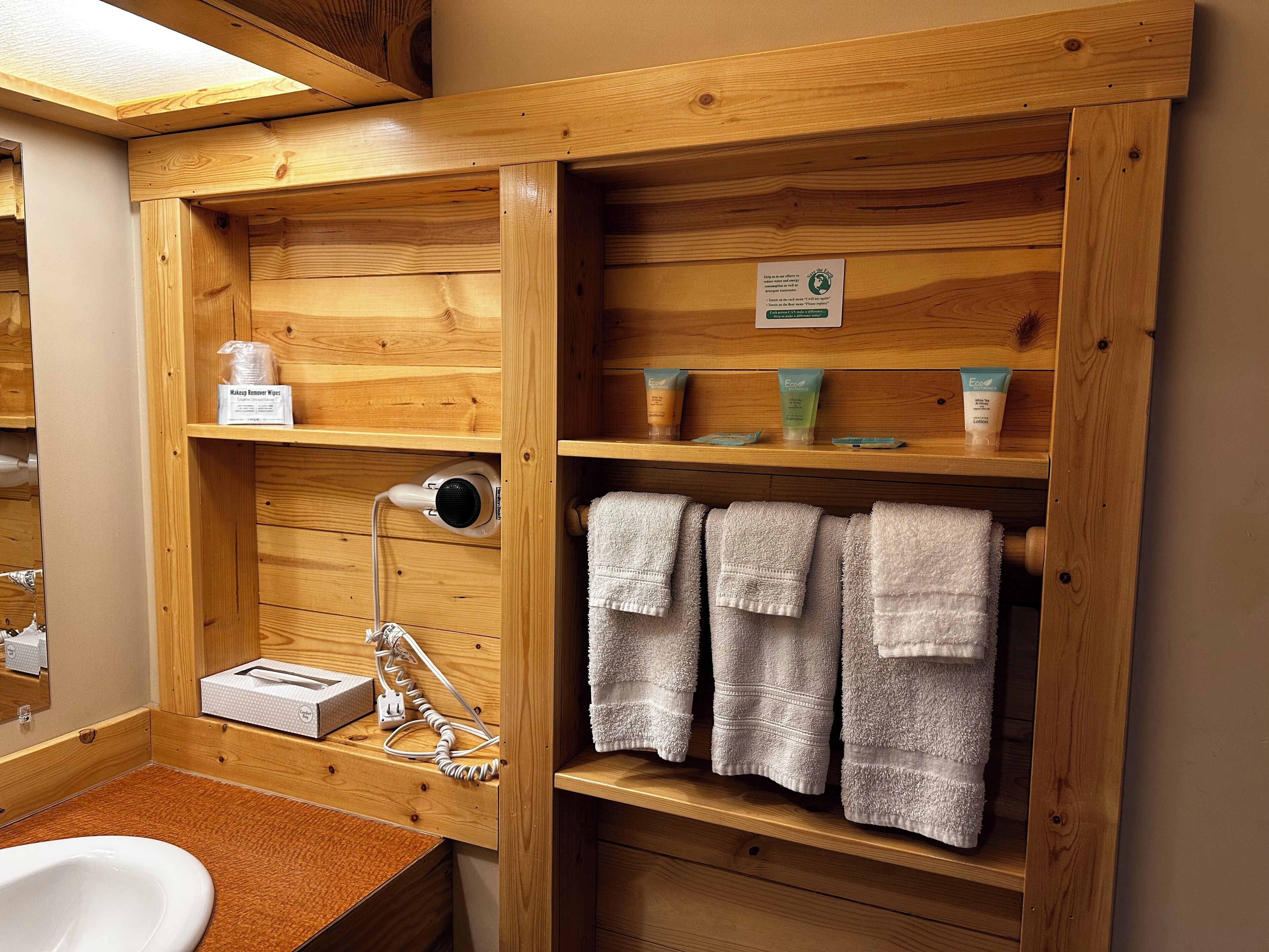 Un baño de madera con lavamanos, toallero y repisas con artículos de aseo.