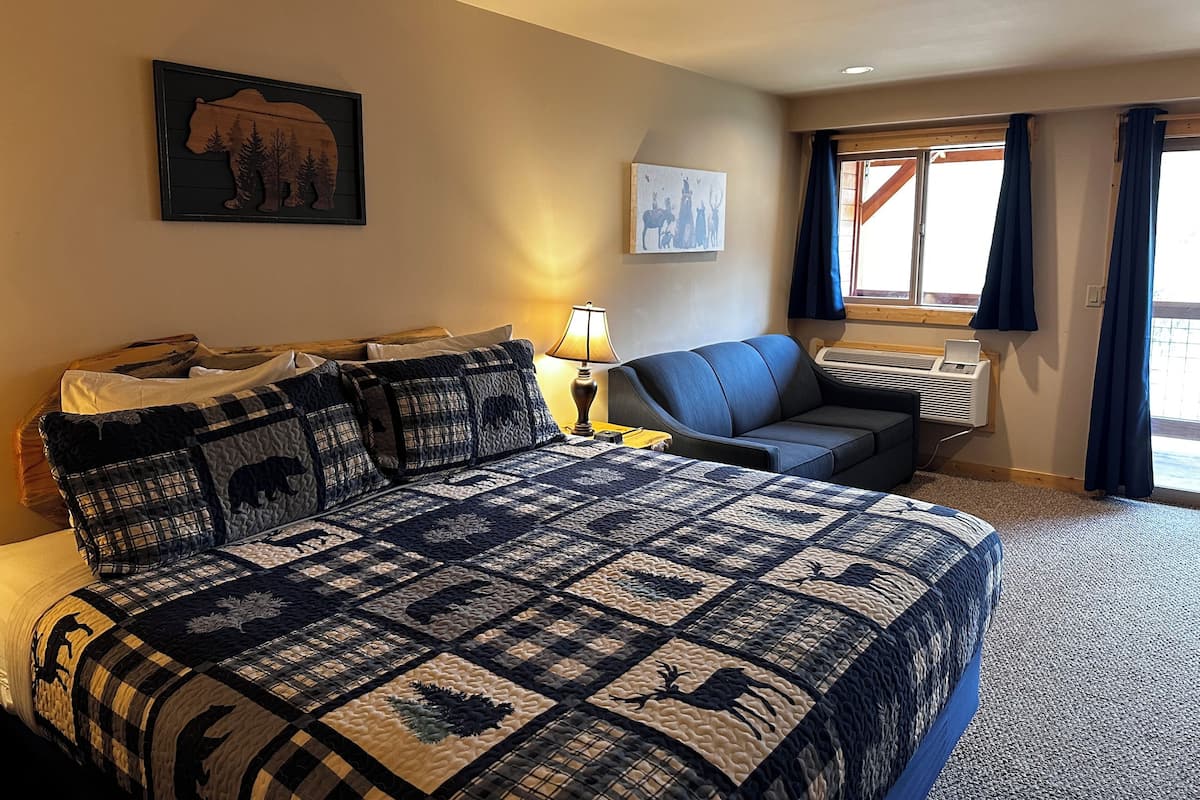 A hotel room with a large bed, a chair, a desk, and a window with curtains.