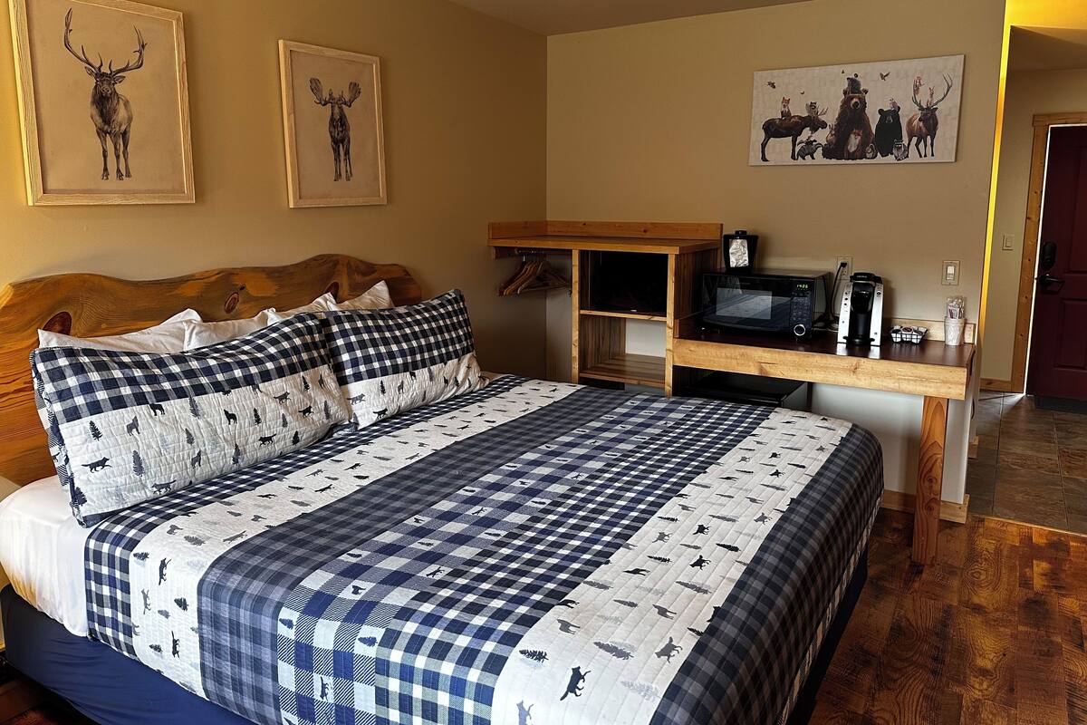 A bedroom with a large bed, a wooden headboard, a desk with a microwave, and artwork on the walls.