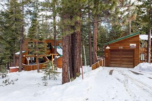 Una cabaña de troncos con garaje, rodeada de nieve y árboles.