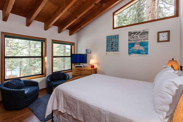 A bedroom with a large bed, two windows, a TV, and artwork on the walls.