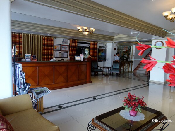 A hotel lobby with a reception desk, seating area, and a staircase.