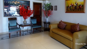 A lobby with a sofa, two chairs, a table with a vase, and a painting on the wall. - Orange Grove Hotel (Davao)