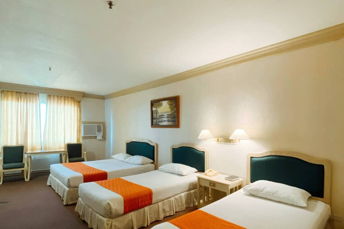 A hotel room with three single beds, a desk, a chair, and a window with curtains.