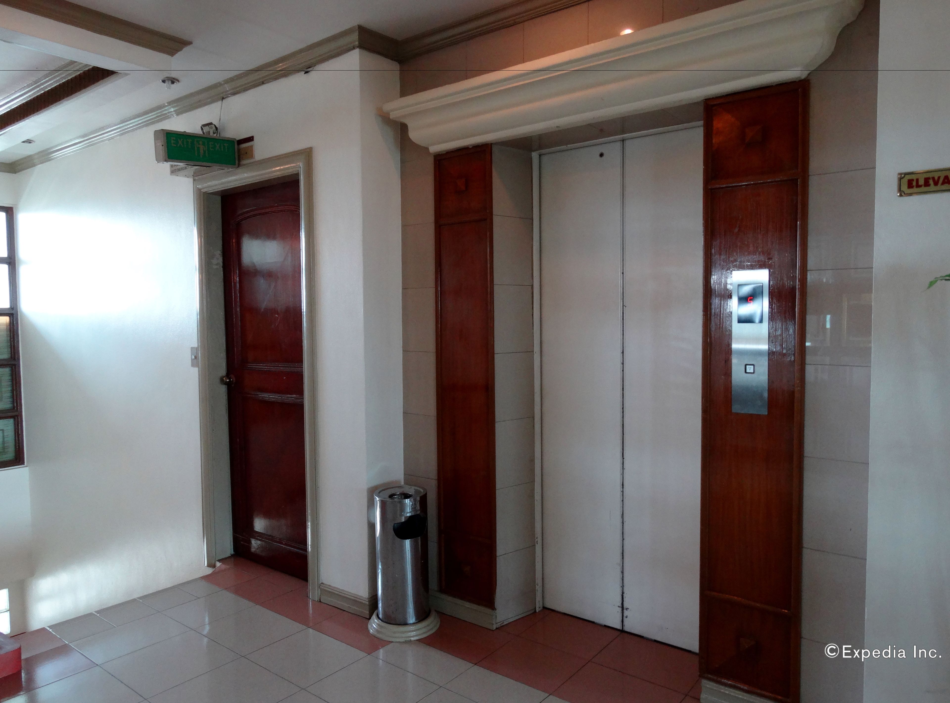 An elevator with a control panel, a trash bin, and a door with a sign indicating an exit.