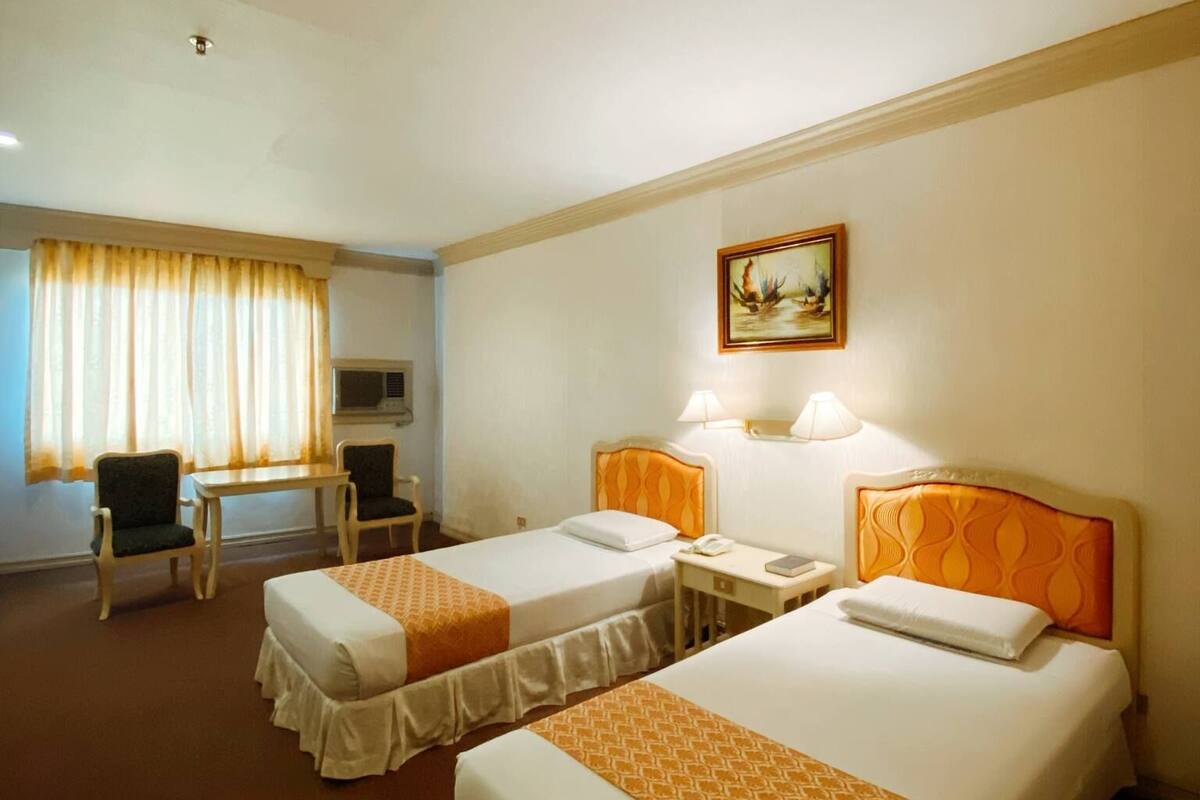 A hotel room with two beds, a desk, a chair, and a painting on the wall.