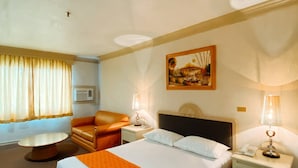 A hotel room with a large bed, a chair, a small table, and a painting on the wall. - Orange Grove Hotel (Davao)