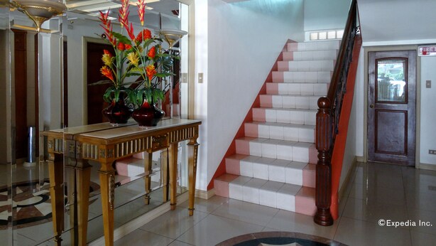A lobby with a staircase, a reception desk, and a large mirror reflecting the decor. - Orange Grove Hotel (Davao)