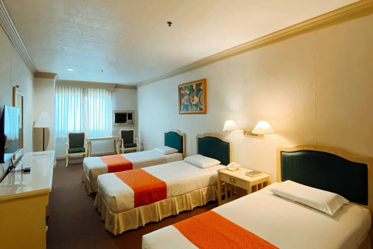 A hotel room with two single beds, a desk, a chair, a television, and a painting on the wall.