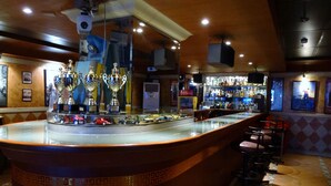 A bar area with a counter displaying trophies and miniature cars, bar stools, and a patterned floor. - Orange Grove Hotel (Davao)