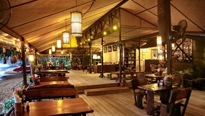 Un restaurante con mesas y sillas de madera, plantas colgantes y una estantería al fondo.