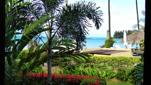 Un resort tropical con un camino que lleva a un área de piscina, rodeado de exuberante vegetación y vistas al océano.