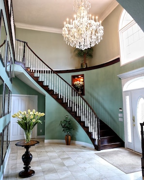 A grand staircase with a chandelier, a vase of flowers, and a framed picture on the wall.
