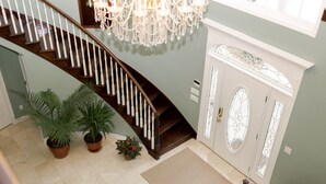 A grand staircase with a chandelier, potted plants, and a door with a decorative glass panel. - Lafayette Grand Manor (Waynesville)