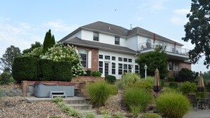 A two-story house with a covered patio area, a small garden with various plants, and outdoor furniture. - Lafayette Grand Manor (Waynesville)