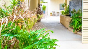 A corridor with a concrete floor, surrounded by various plants and a stone wall. - Atlantic West Beach Apartments (West Beach)