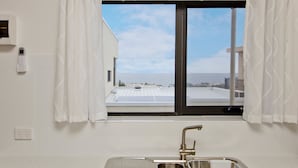 A modern kitchen with a stainless steel sink, a window with curtains, and a view of the sea. - Atlantic West Beach Apartments (West Beach)