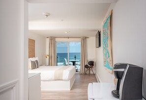 A hotel room with a bed, a desk, a chair, a coffee maker, a TV, and a view of the ocean.